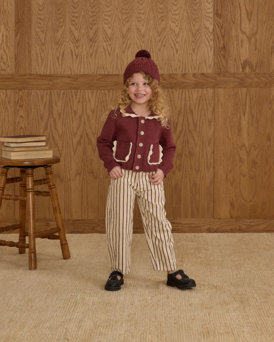 Child wearing a maroon outfit with a striped pattern against a wooden paneled wall.