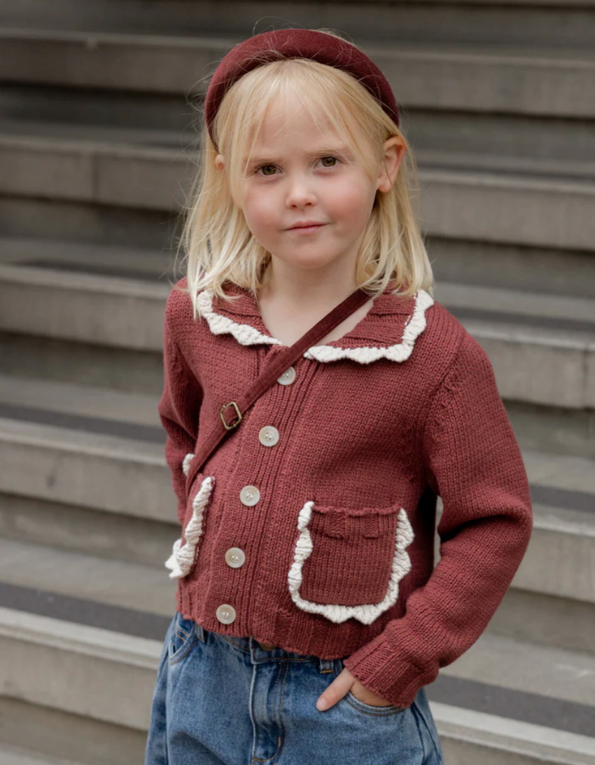 Young girl wearing a red knitted cardigan with white trim, standing on steps.